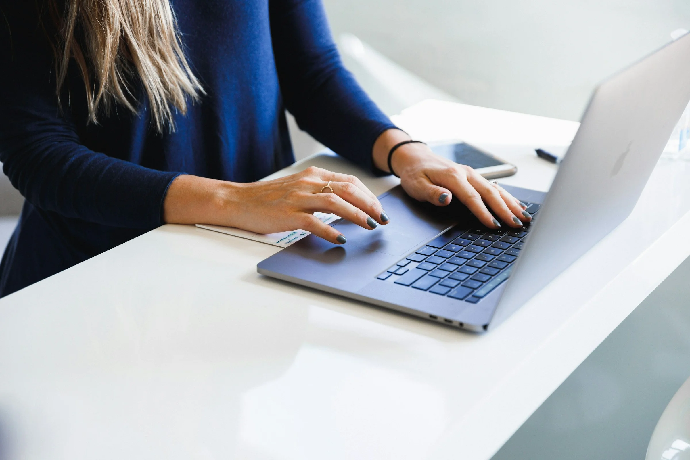 A woman typing on a laptop at a white desk.